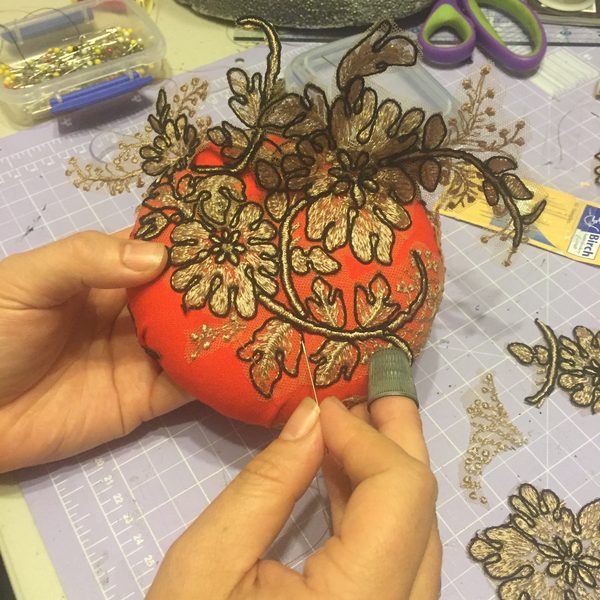 Hands stitching gold lace onto an orange fascinator