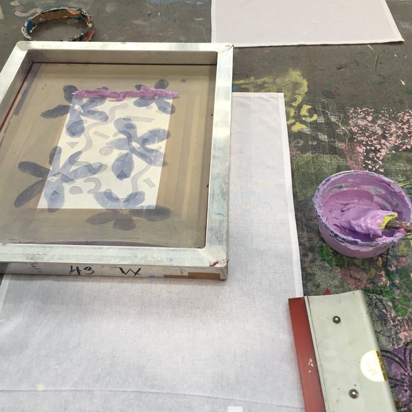 A screen printing frame with a floral design and a tub of purple ink