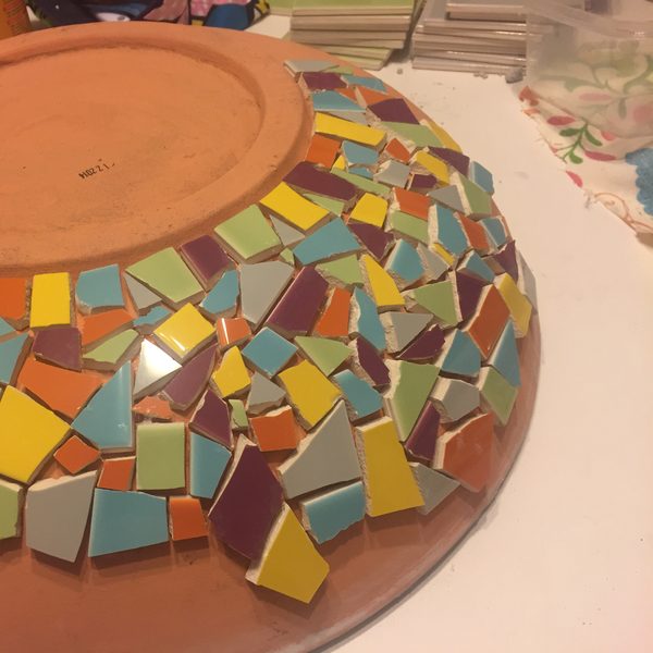 A terracotta bowl half covered in colourful mosaic tiles