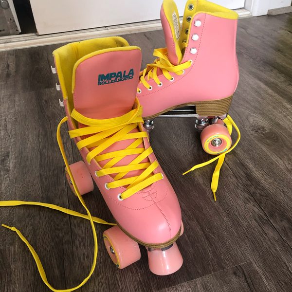 A pair of pink roller skates with yellow laces