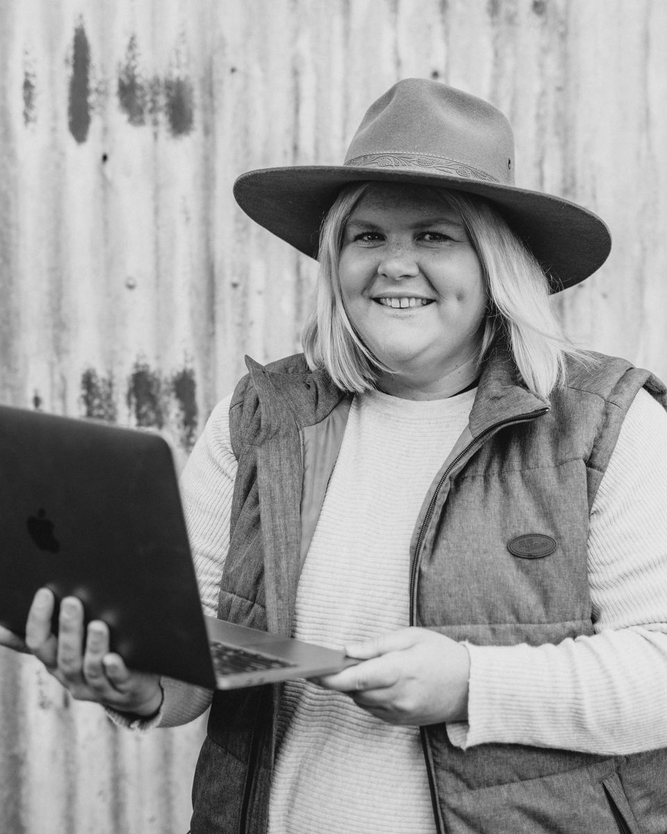 Nikki Davey in a wide-brimmed hat, smiling and holding a laptop