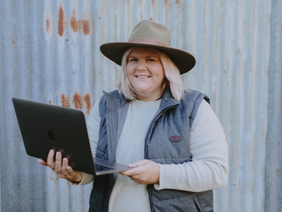 Nikki holding up a laptop in front of a corrugated iron wall