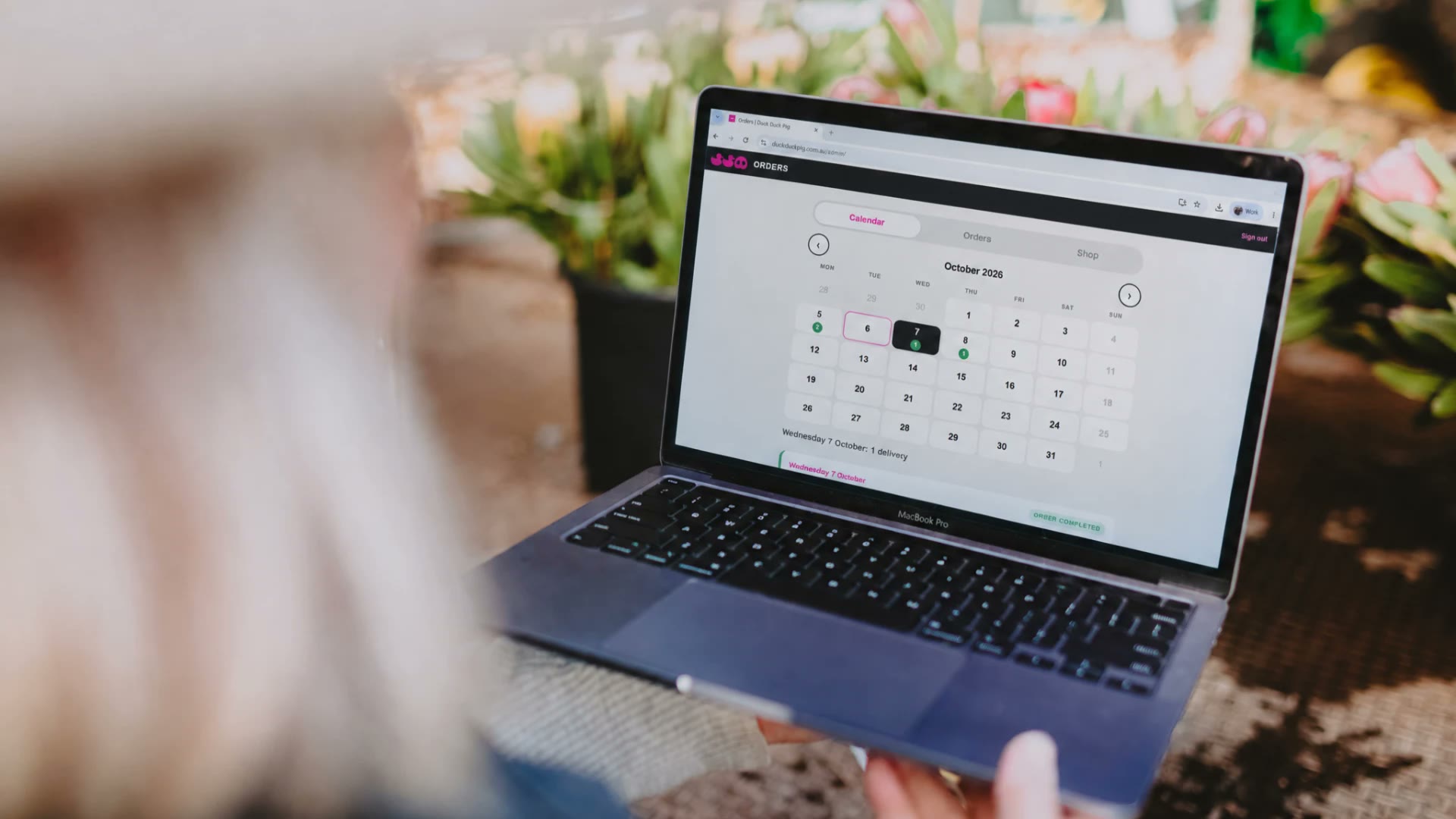 Nikki looking at the DDP Orders delivery calendar on a laptop, with tulips in the background